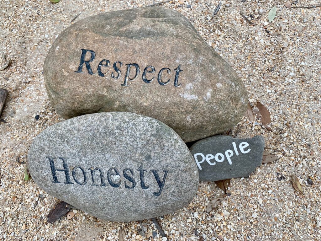 Three stones or rocks sitting in a garden with the words respect, honesty, and people
